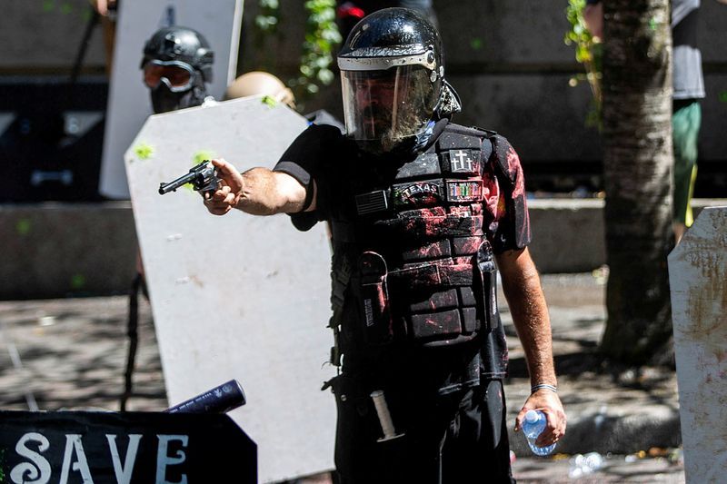 Alan Swinney takes aim at protesters with a revolver, finger on trigger and hammer pulled back